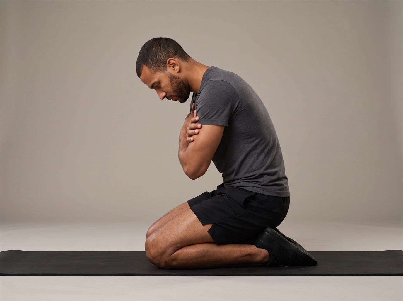 A man kneeling on a mat, hips folded back toward his heels and his upper back rounded, head down — the hips-folding error that removes the load from the quads in a reverse Nordic.