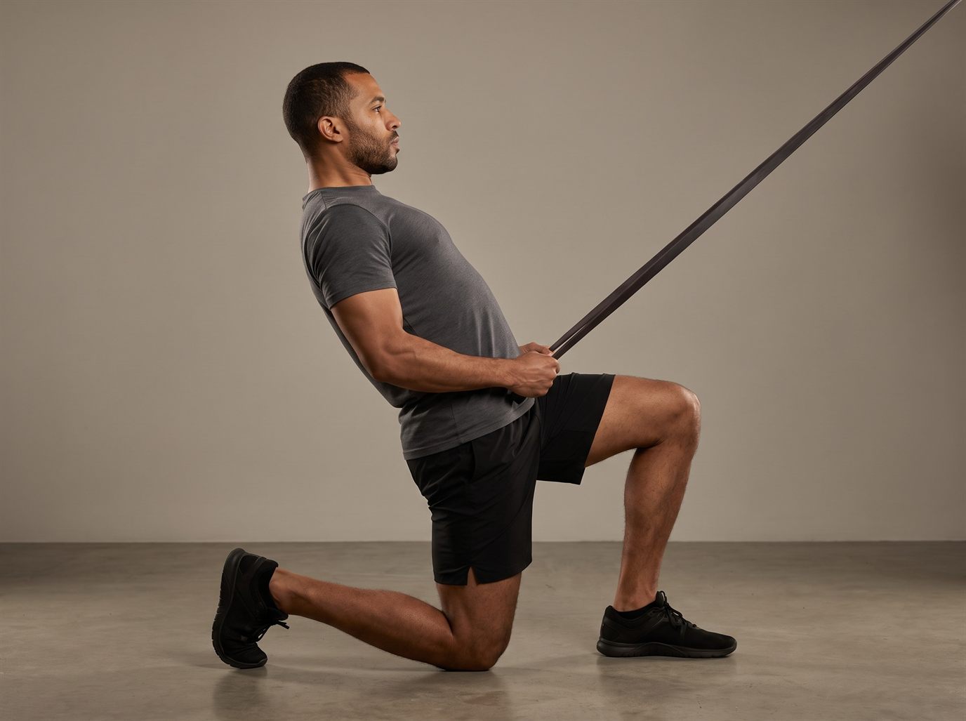 A man half-kneeling during a band lat pulldown alternative with his torso leaning well back past vertical, ribs flared and lower back arched, pulling the band toward his waist instead of drawing it down.